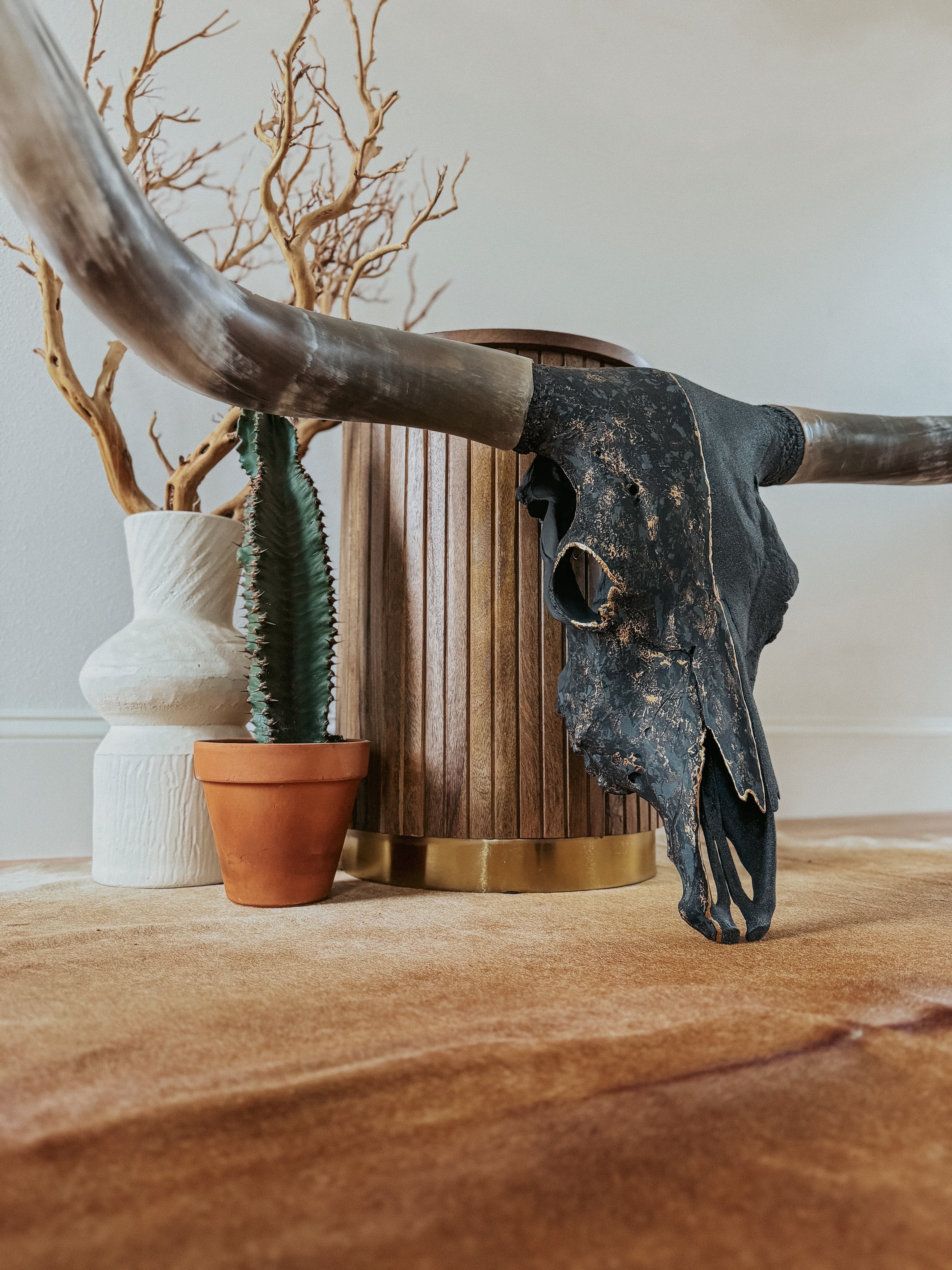 Black and gold painted longhorn cow skull leaning on wood stool on floor