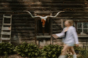 Blurry slow exposure of a women walking past a longhorn cow skull on an old log cabin