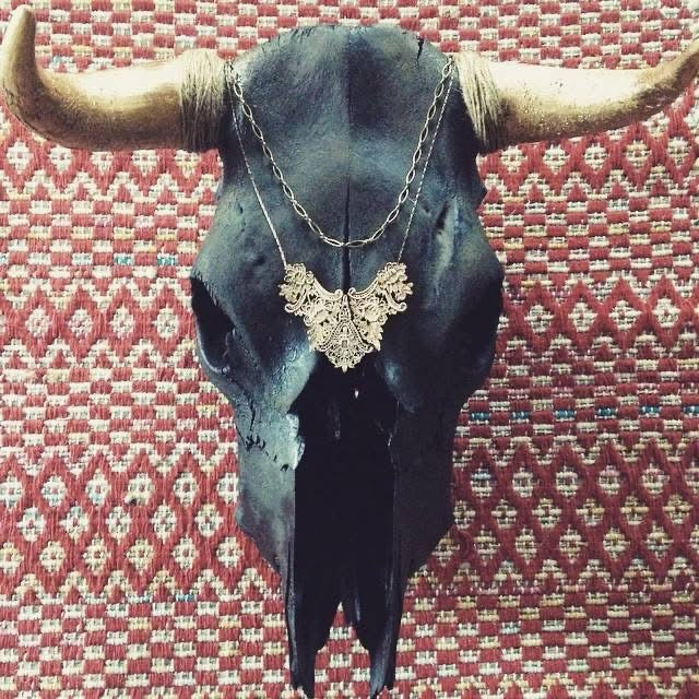 Black painted American buffalo skull with gold painted horns and gold necklace over red and white diamond patterned rug