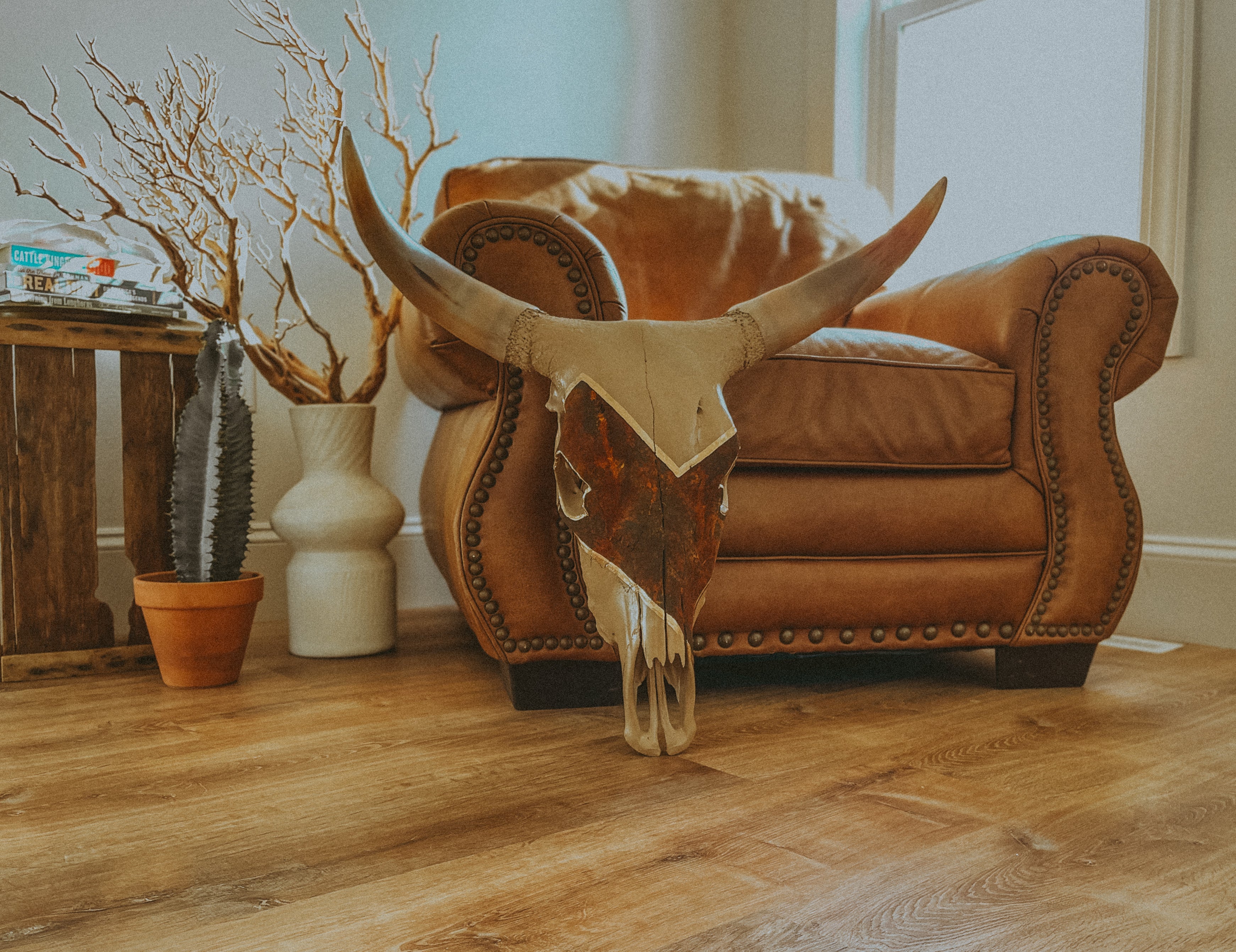 Custom designed cow skull painted tan with diagonal rust pattern leaning on a leather chair