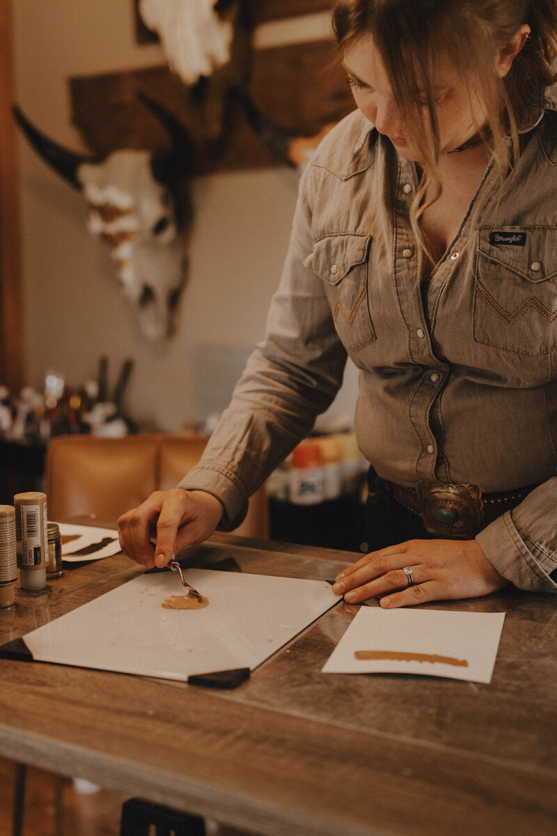 Wanderlust skulls owner working at a table mixing colors with a pallet knife, in a room with rustic decor.